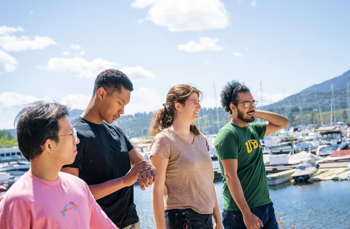 Four students standing in a shipyard, looking out toward the water.
