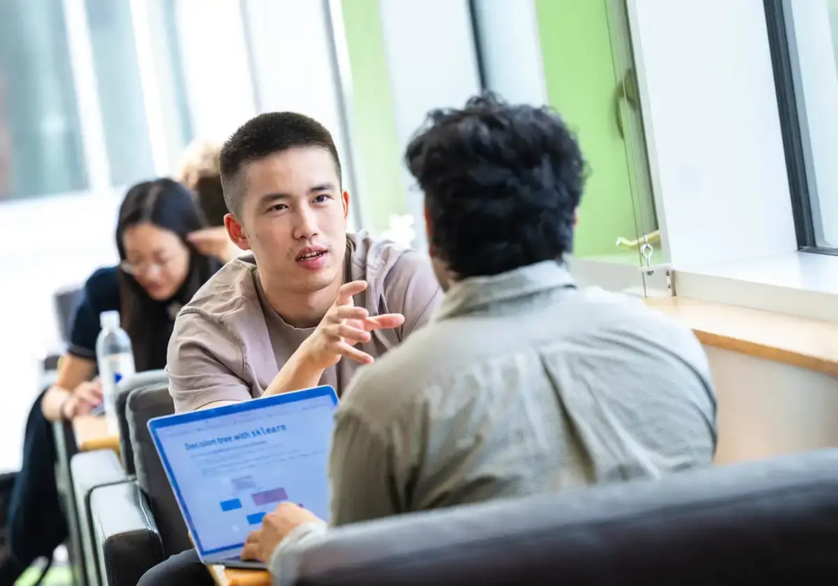 Two UBC students sit facing each other in a bright study space, engaged in a focused conversation.