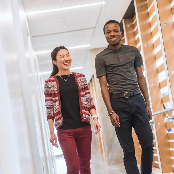 Two students walking and talking down a hallway.
